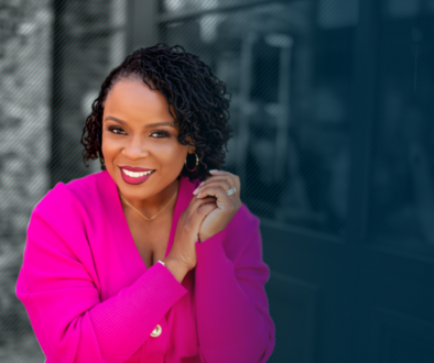 Dr. Amber L. Wright standing on the left side of the frame wearing a pink power suit and looking at the camera with a smile