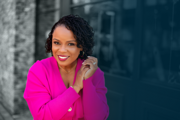 Dr. Amber L. Wright standing on the left side of the frame wearing a pink power suit and looking at the camera with a smile