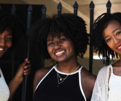 3 Black women with natural hair shown from the chest up, smiling at the camera