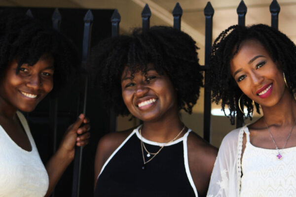 3 Black women with natural hair shown from the chest up, smiling at the camera