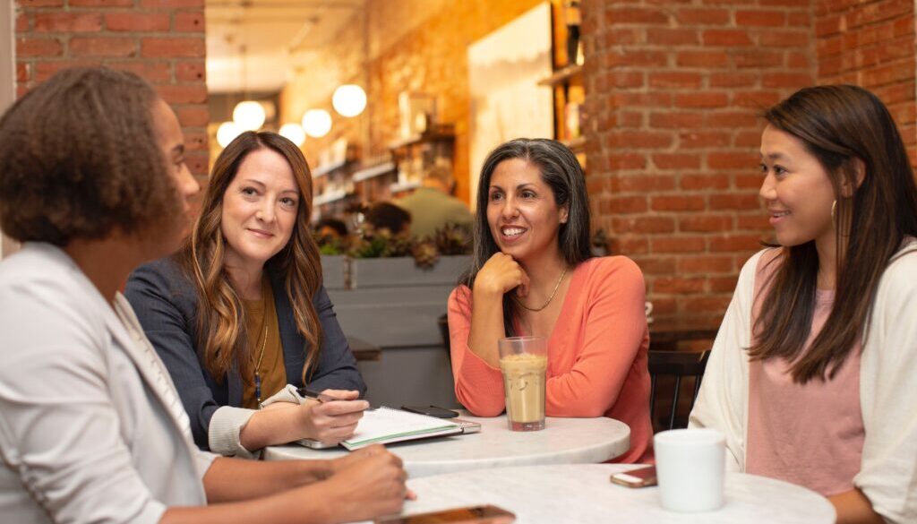 Four women sitting around a table facing each other and deep in a conversation.